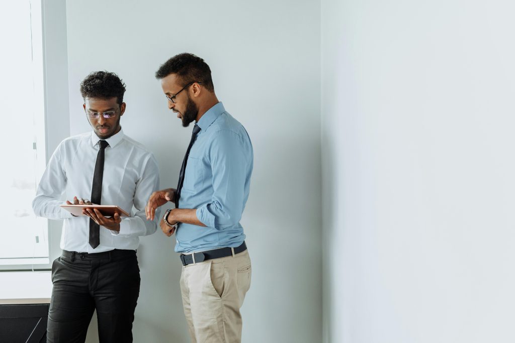 Two businessmen discussing work with a tablet against a white wall in a modern office setting.